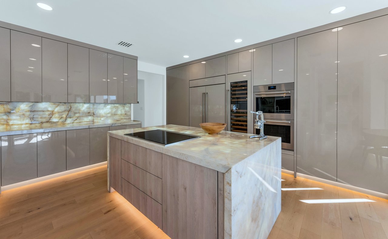 Modern kitchen with a veined stone island, glossy taupe cabinets, and built-in wine cooler.
