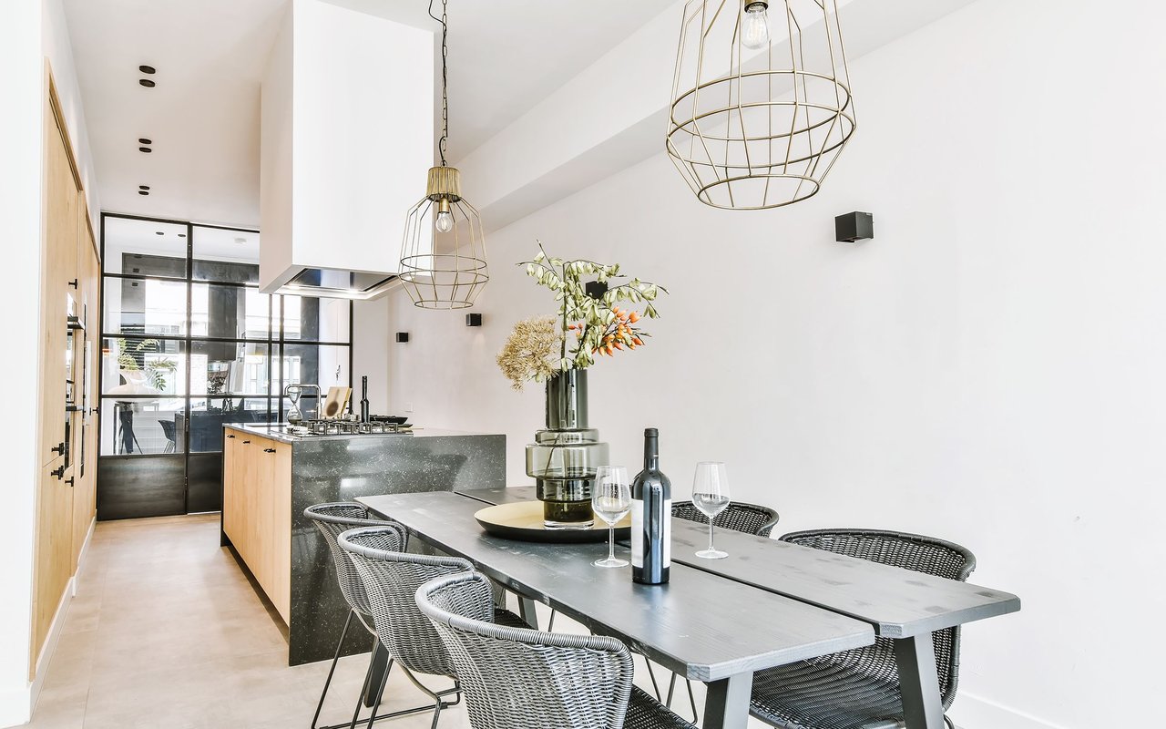 Modern kitchen and dining area with a gray island, light wood cabinets, and a long table with woven chairs.