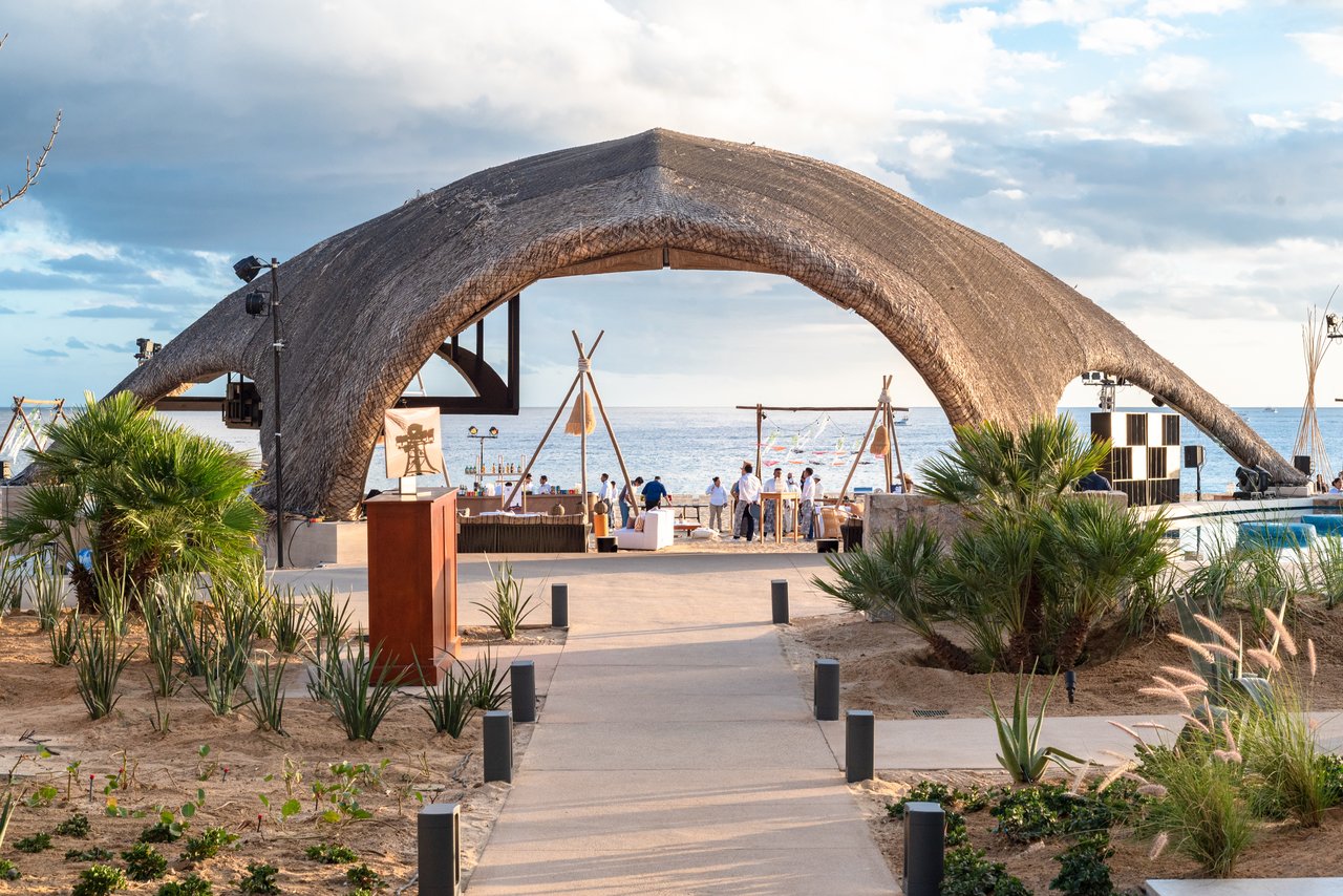 Thatched archway at Quivira’s beachfront club, framing an oceanfront terrace and gathering area.