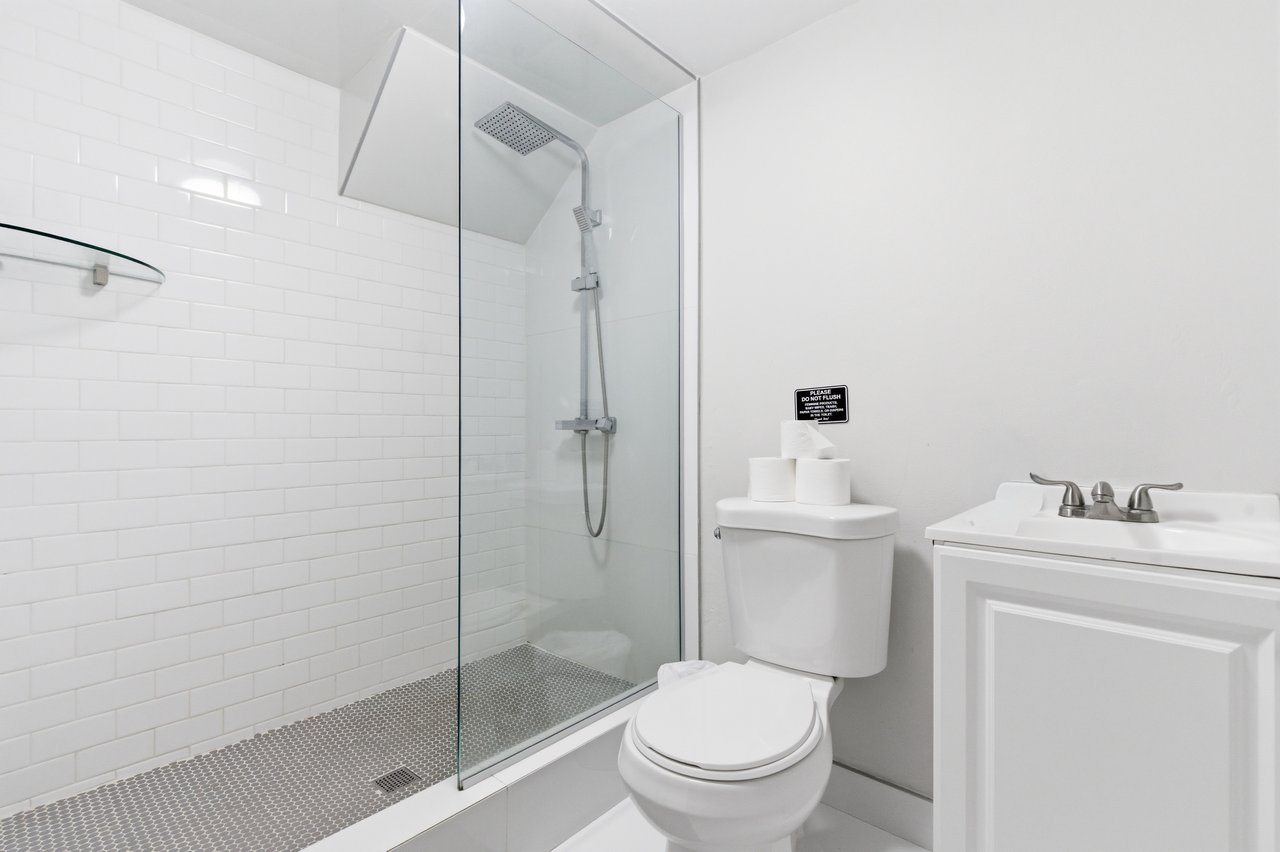 Bathroom with a glass walk-in shower, white subway tile, mosaic floor, toilet, and vanity.