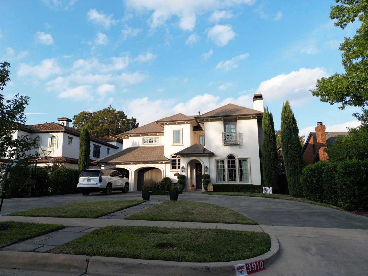 White two-story home with a tiled roof, arched entry, three-car garage and SUV in the driveway.