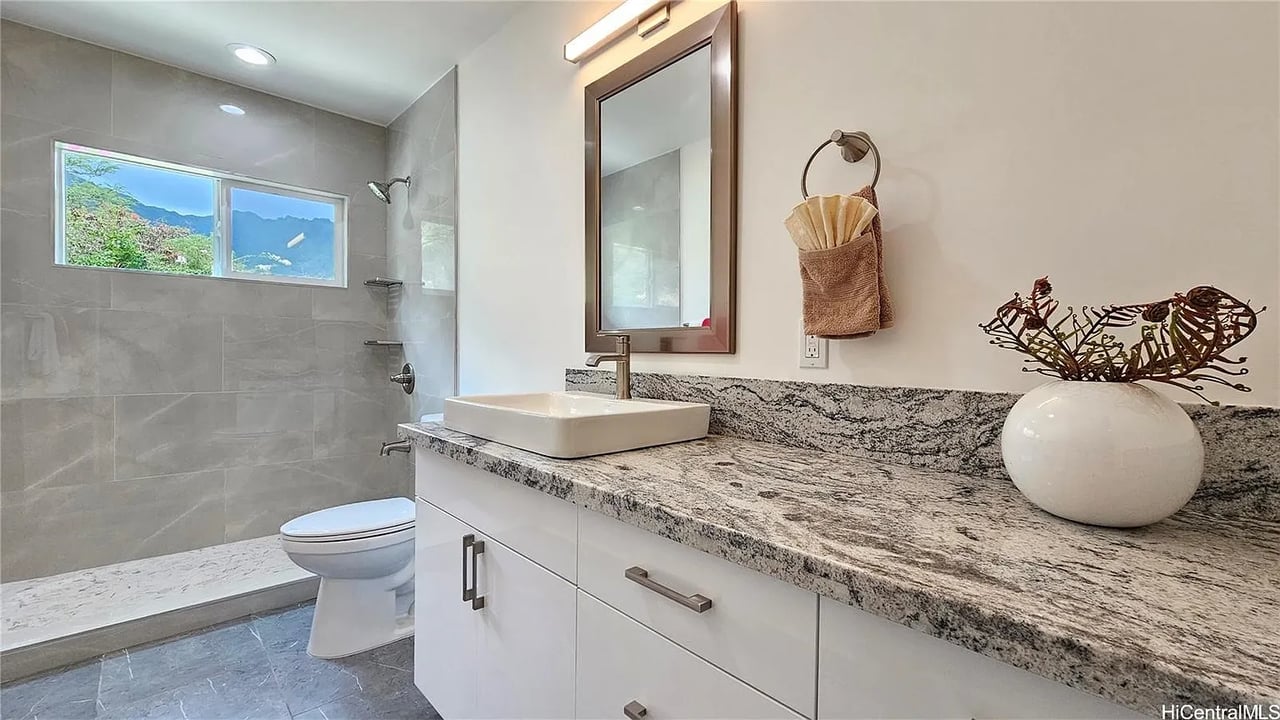 Bathroom with a granite vanity and vessel sink beside a gray-tiled shower overlooking mountains.