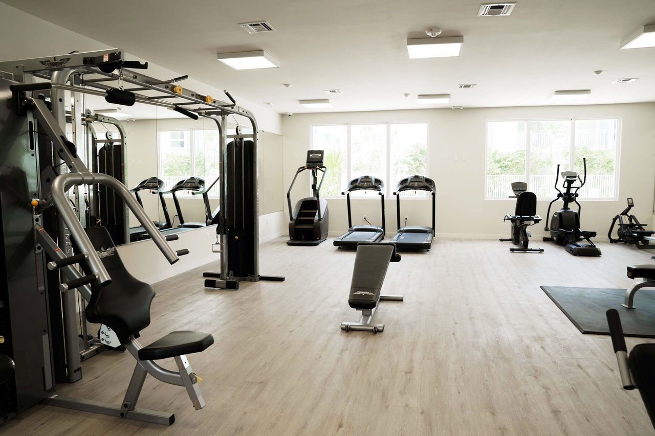 Fitness room with weight machines, treadmills, and stationary bikes by large windows.