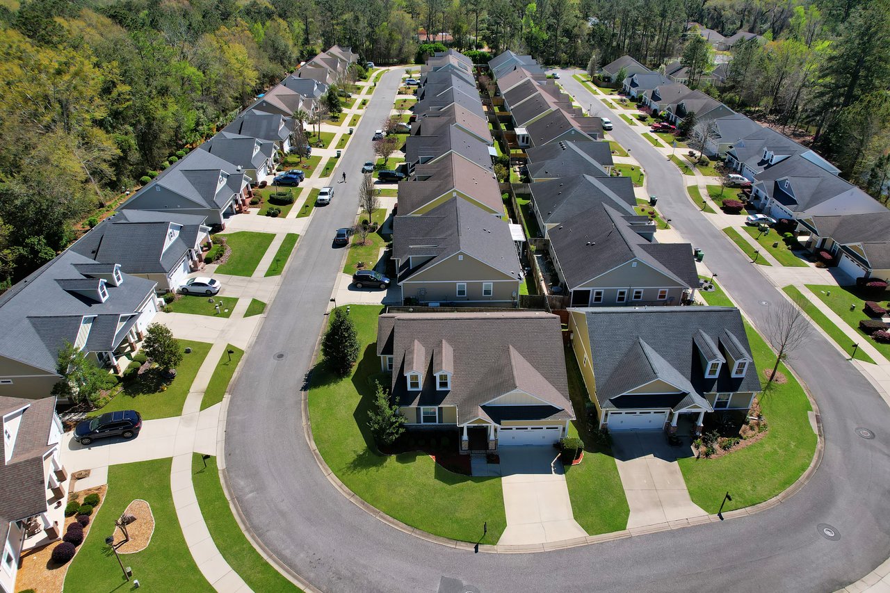 Aerial view of a suburban neighborhood with rows of identical houses. Neatly trimmed lawns line the streets, conveying a sense of order and calm.