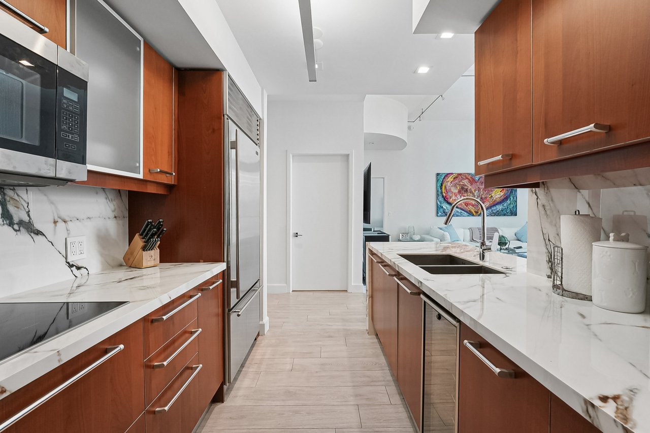 Refreshed kitchen with wood cabinetry, marble-pattern counters and stainless appliances in Jade at Brickell Bay Unit 611