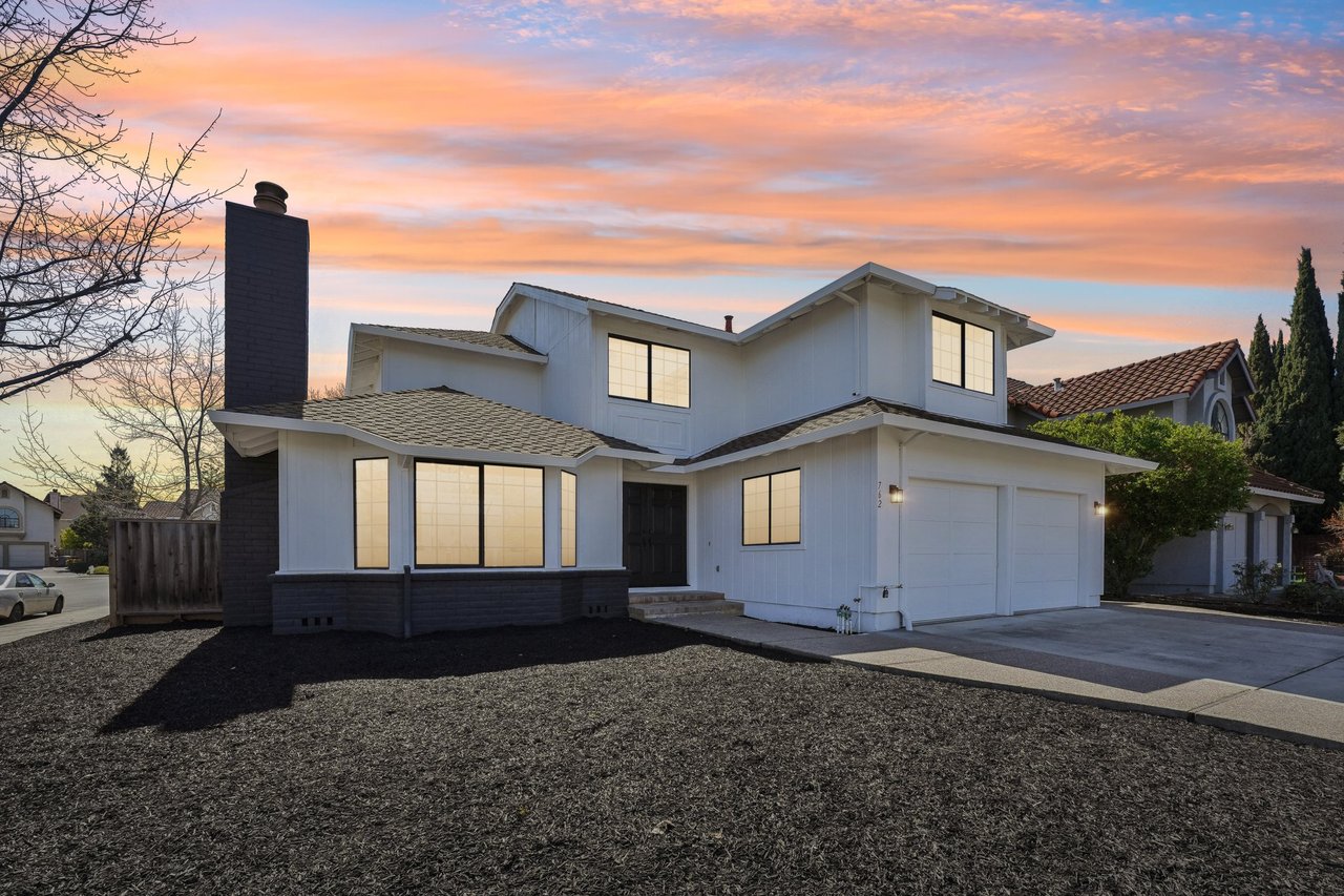 Two-story white house with a dark chimney and glowing windows at sunset.