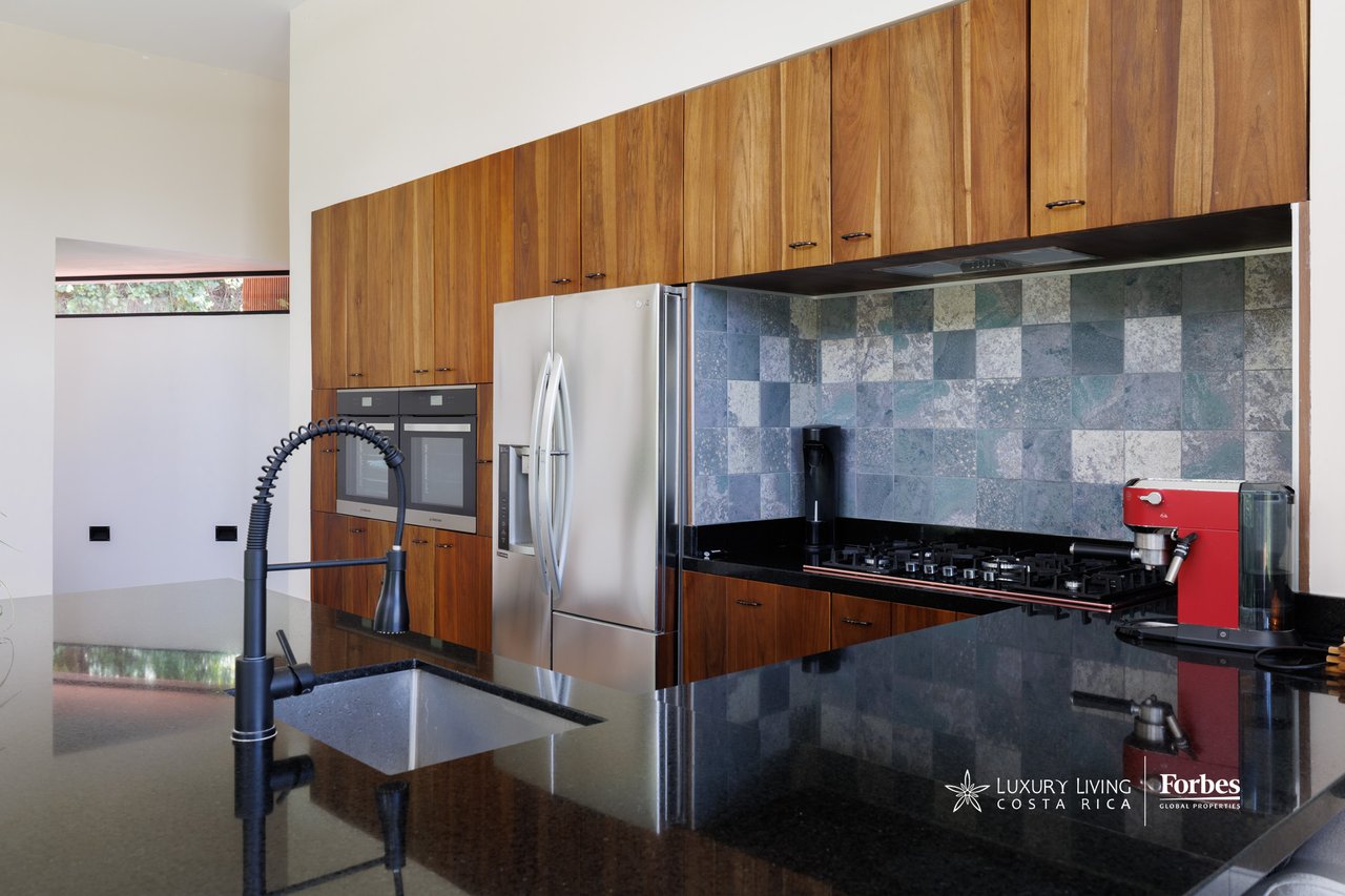Modern kitchen with warm wood cabinets, stone-tile backsplash, and a black island with an integrated sink.