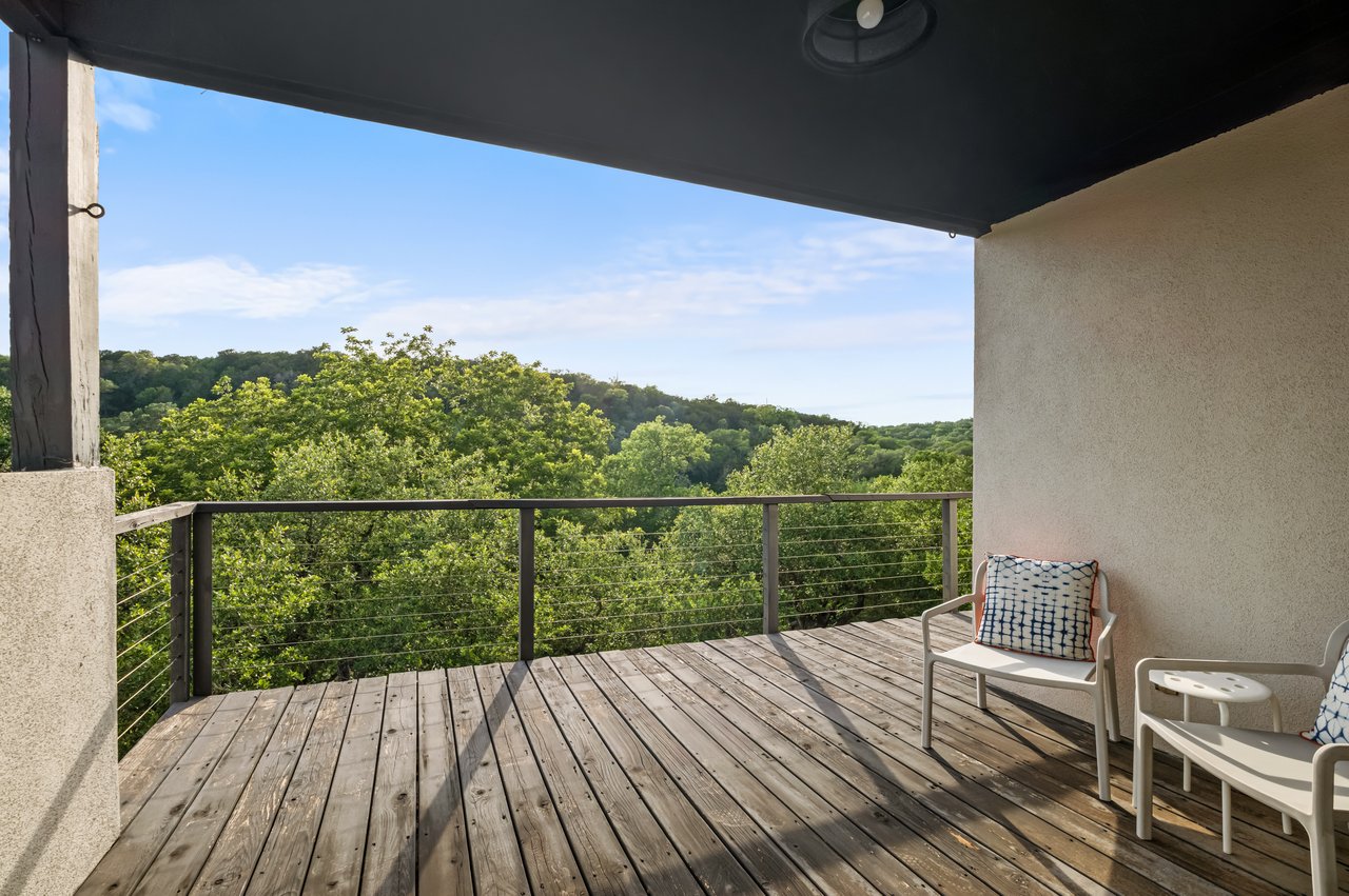 Wooden balcony with white chairs overlooking wooded hills.
