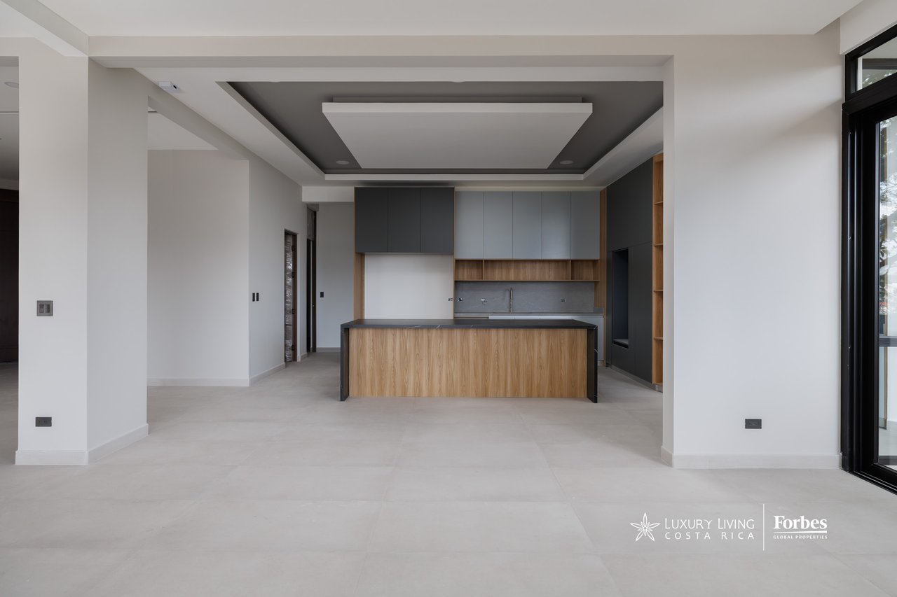 Modern apartment kitchen with a wood-fronted island, gray cabinetry, and large black-framed windows.