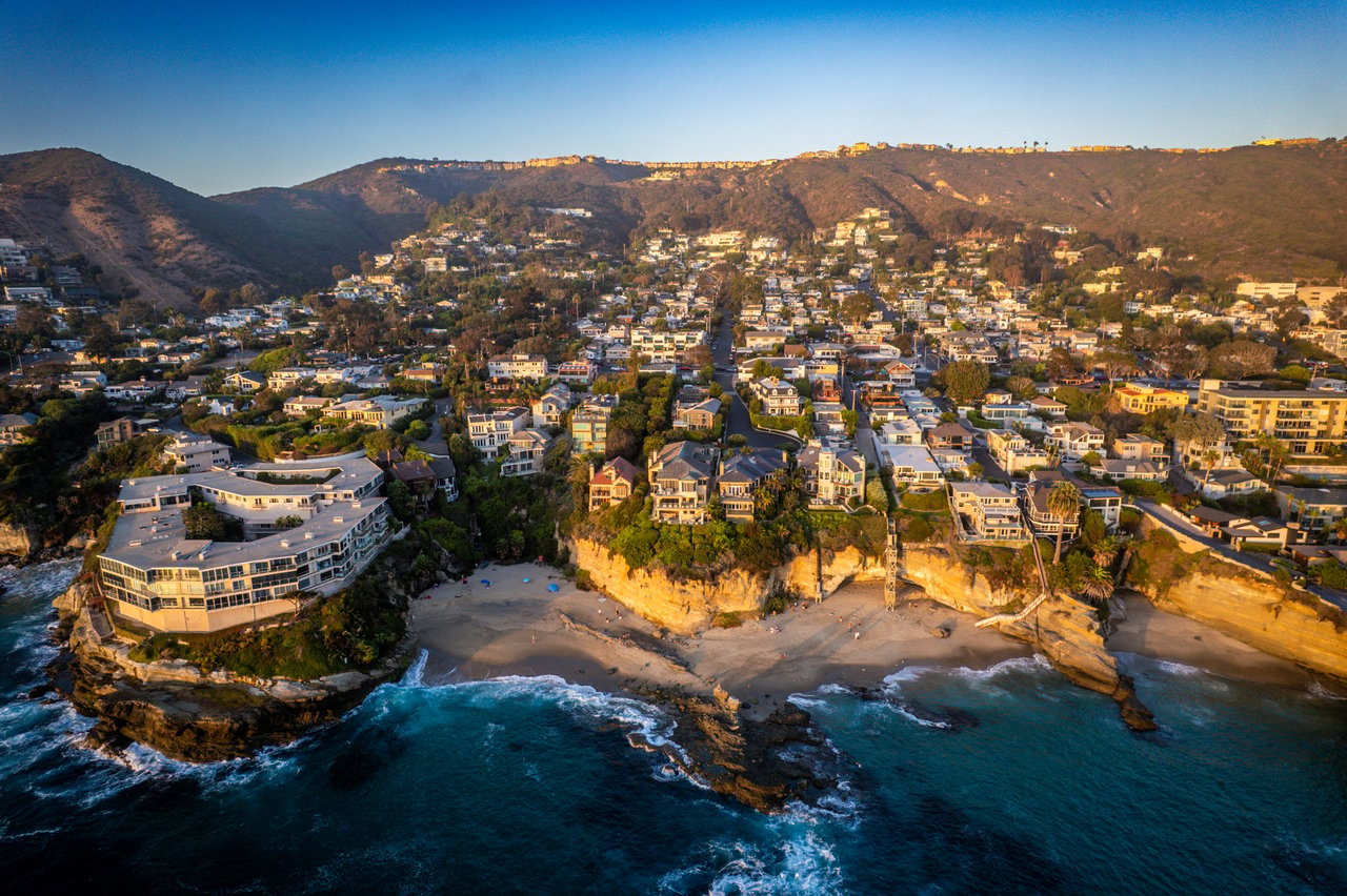 Coastal neighborhood on rugged cliffs above a beach and ocean at golden hour.