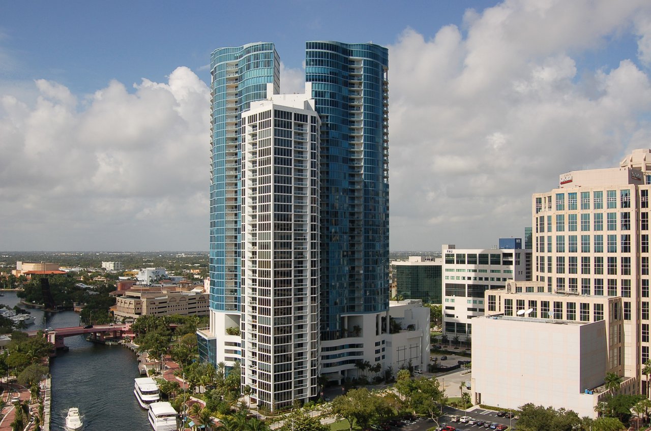 Curved blue-glass condominium tower overlooking a canal and downtown buildings.