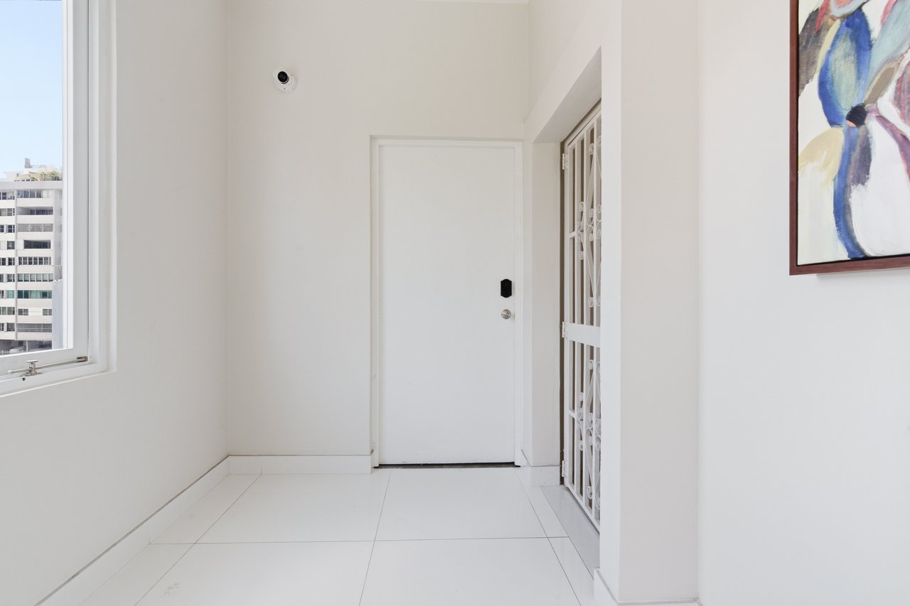 White apartment entry hall with tiled floor, security gate, and a large window overlooking a neighboring building.