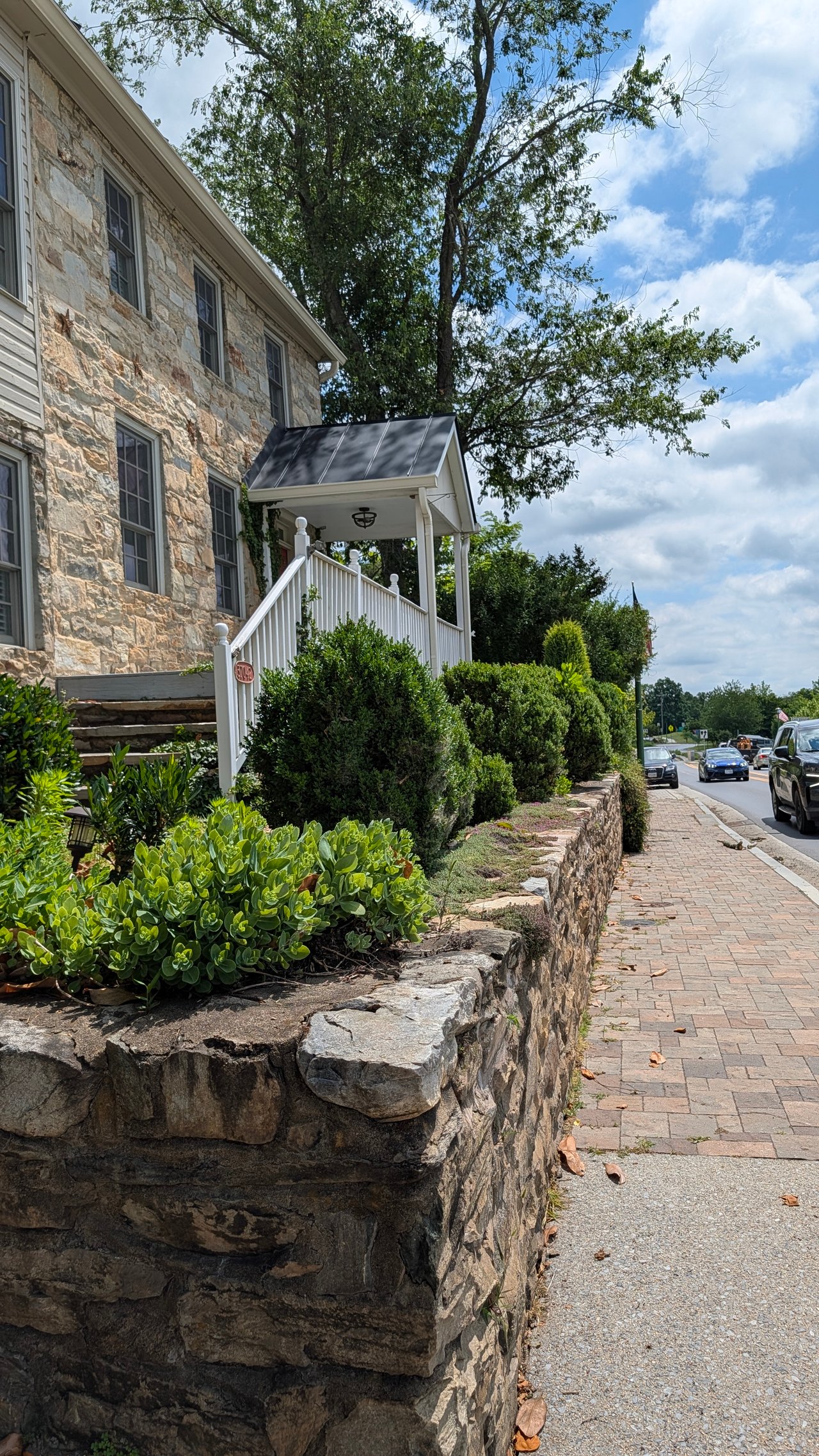 A close-up view of a historic dry-stack fieldstone retaining wall running alongside a newly updated brick paver pedestrian sidewalk in Hillsboro, VA, documented by local real estate expert Diane Geremia.