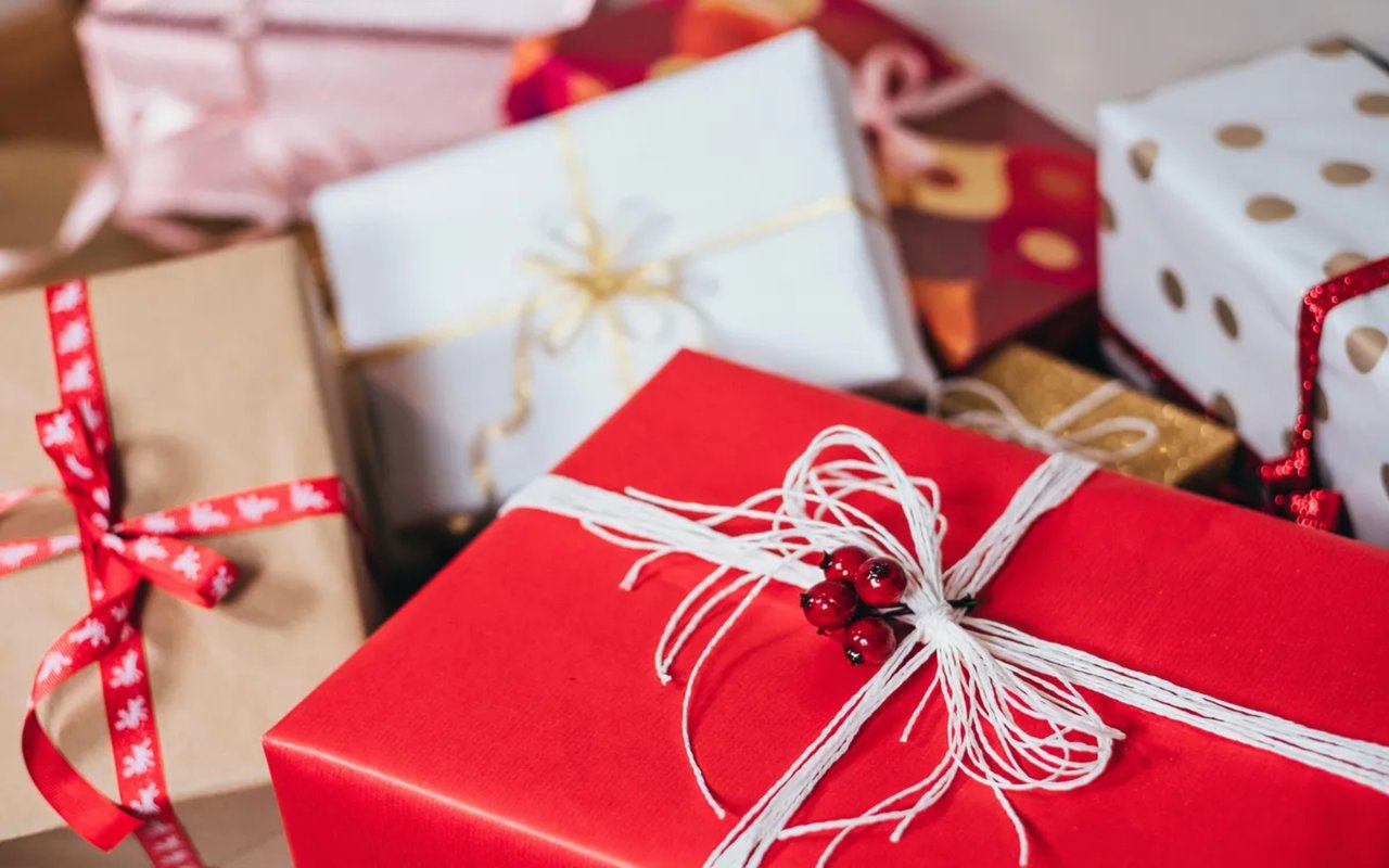 A festive pile of wrapped holiday gifts, with a red gift box decorated with white twine and red berries in the foreground.