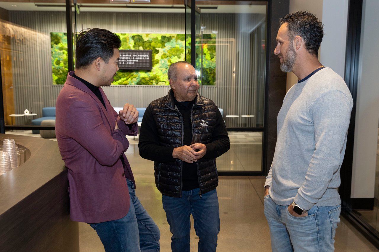Three men talk inside a modern venue, with a green living wall behind them.
