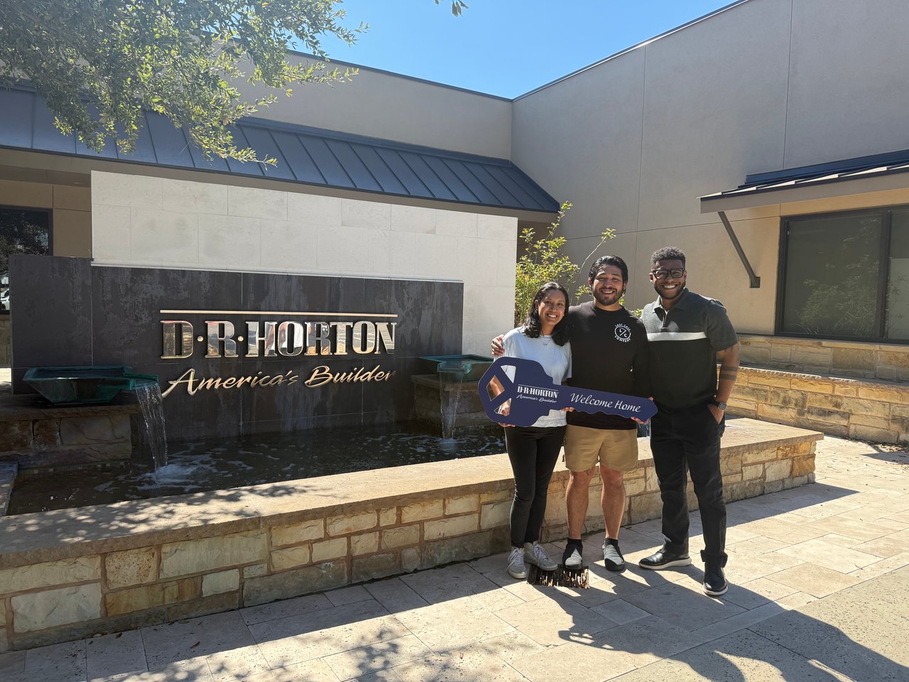 Three people celebrate outside a D.R. Horton building while holding a Welcome Home key.