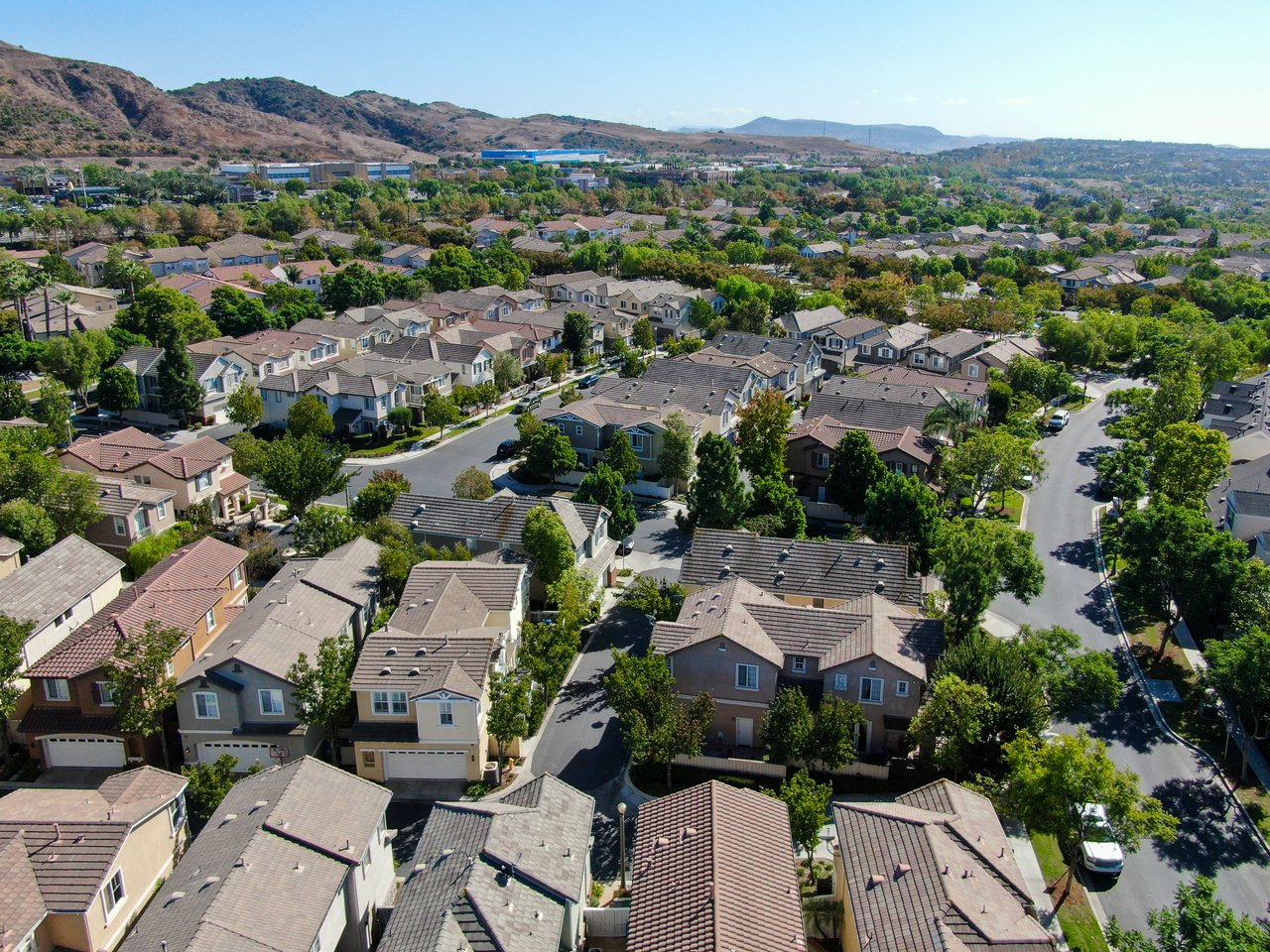Aerial view of a residential neighborhood with tree-lined streets and rolling hills beyond.