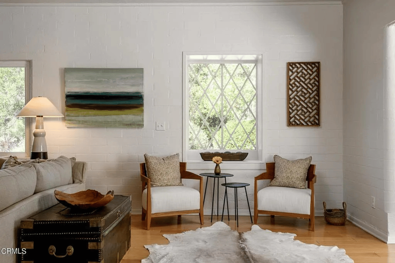 Living room with white brick walls, a diamond-pane window, and two wood-framed armchairs.