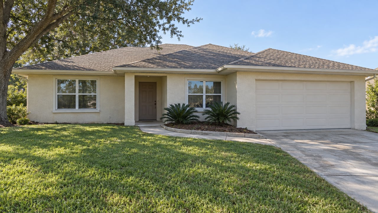 An established single-story stucco home with a shallow shingle roof, deep front lawn, curved concrete approach and mature live oak.