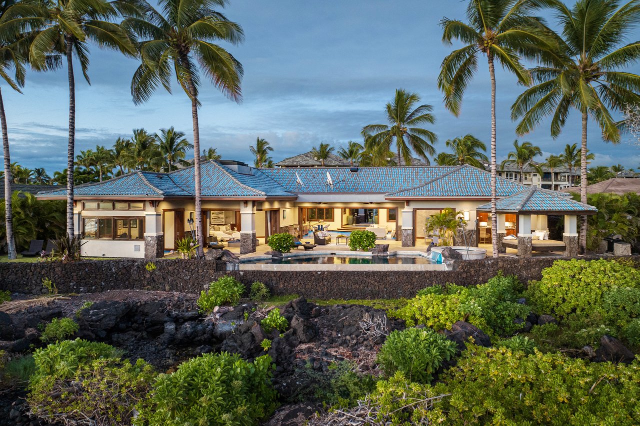Hawaiian-style home with a blue tile roof, pool, and tall palm trees.