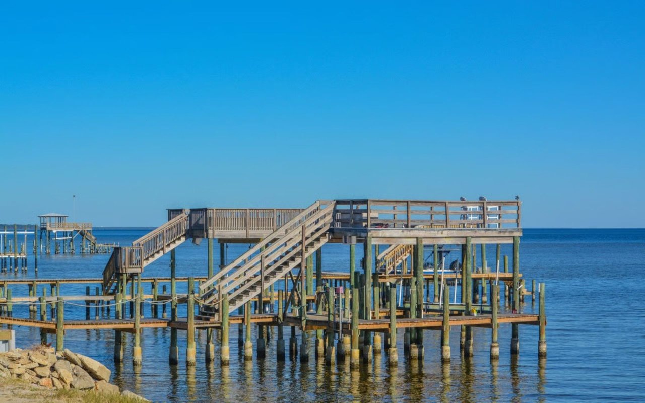 Wooden boardwalks and viewing platforms extend over calm coastal water beside a rocky shoreline.