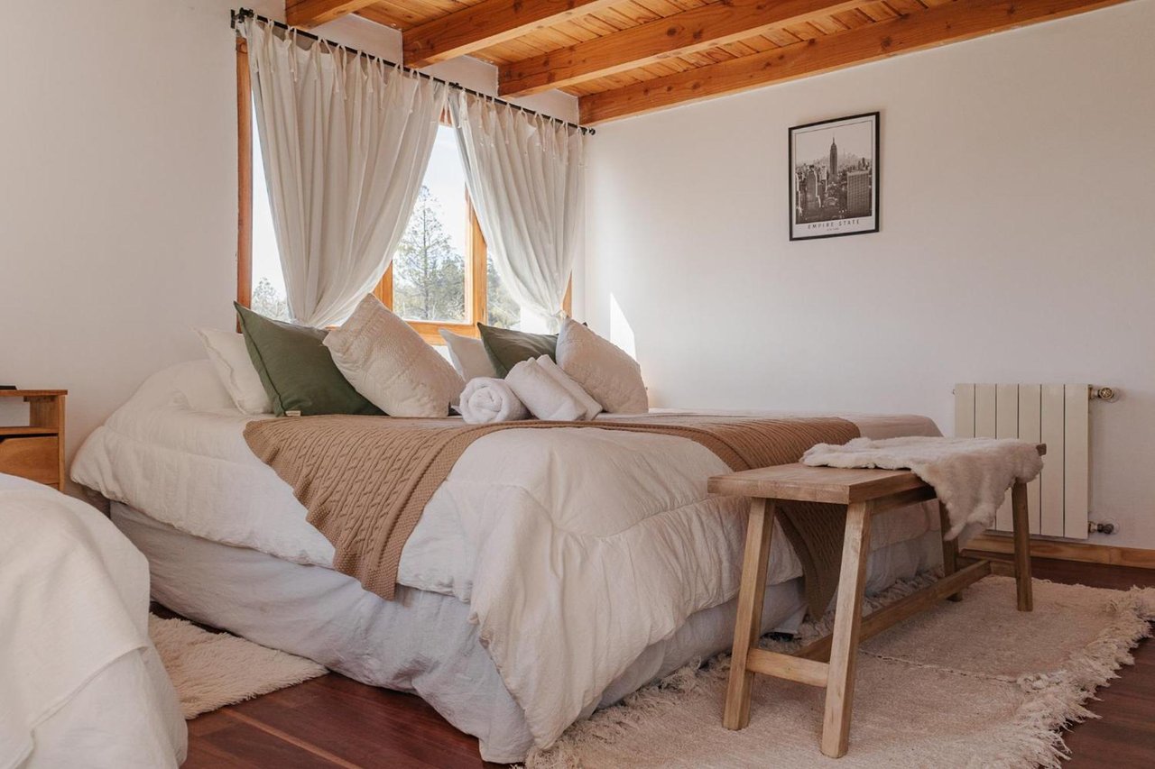 Boutique hotel bedroom with a white bed, folded towels, wooden ceiling, and curtained window.