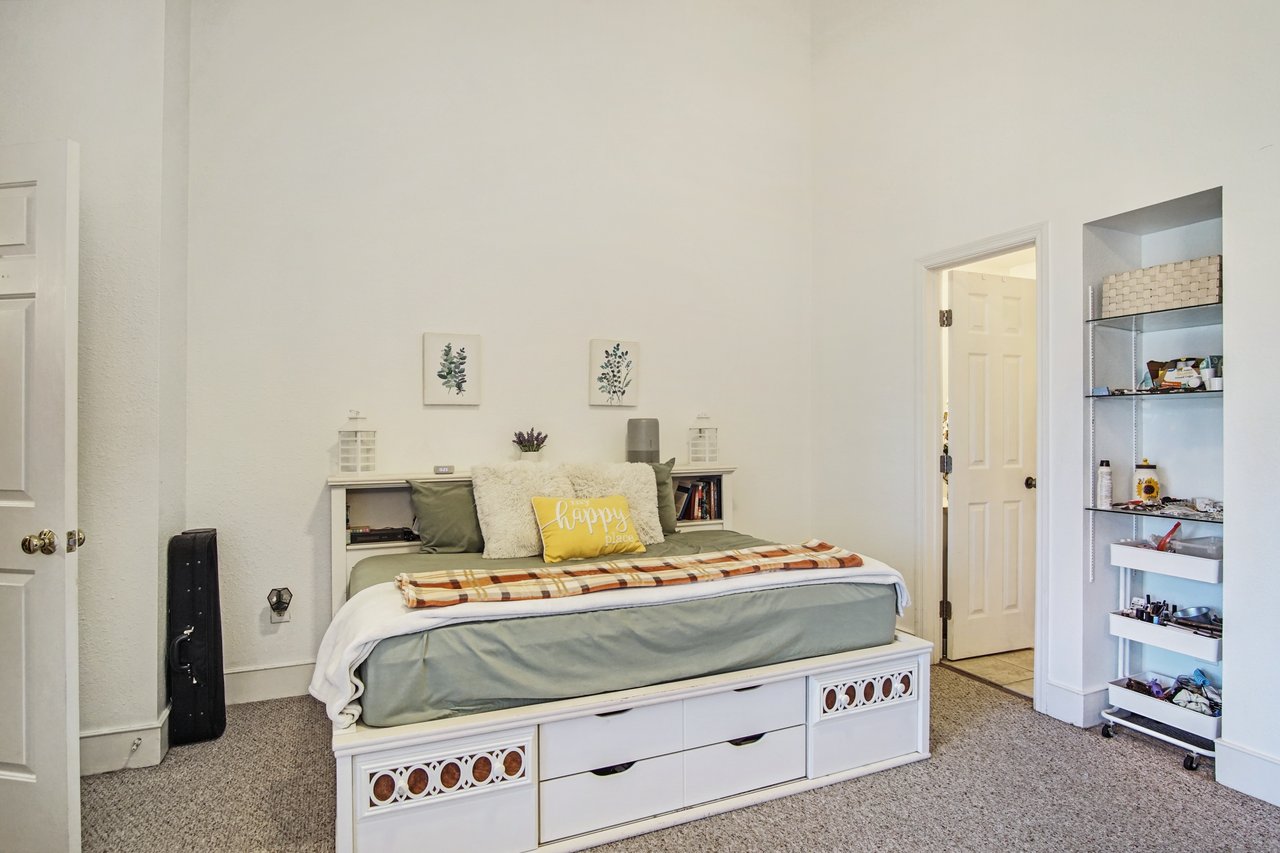 Cozy bedroom with a white storage bed, sage green bedding, and a yellow "happy place" pillow. Wall art and decorative lanterns add charm, with a soft ambiance.