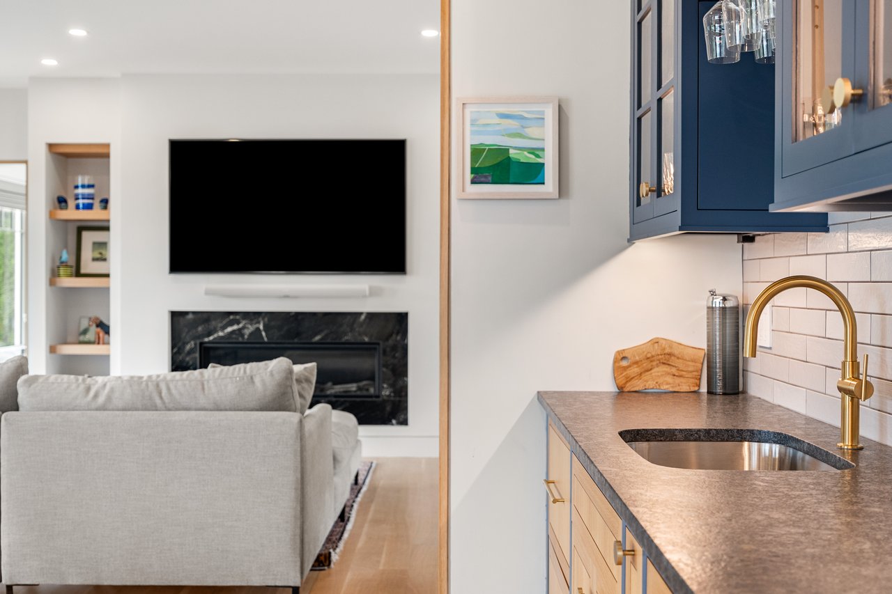 Open-plan kitchen and living room with blue cabinets, a brass faucet, and a marble fireplace.