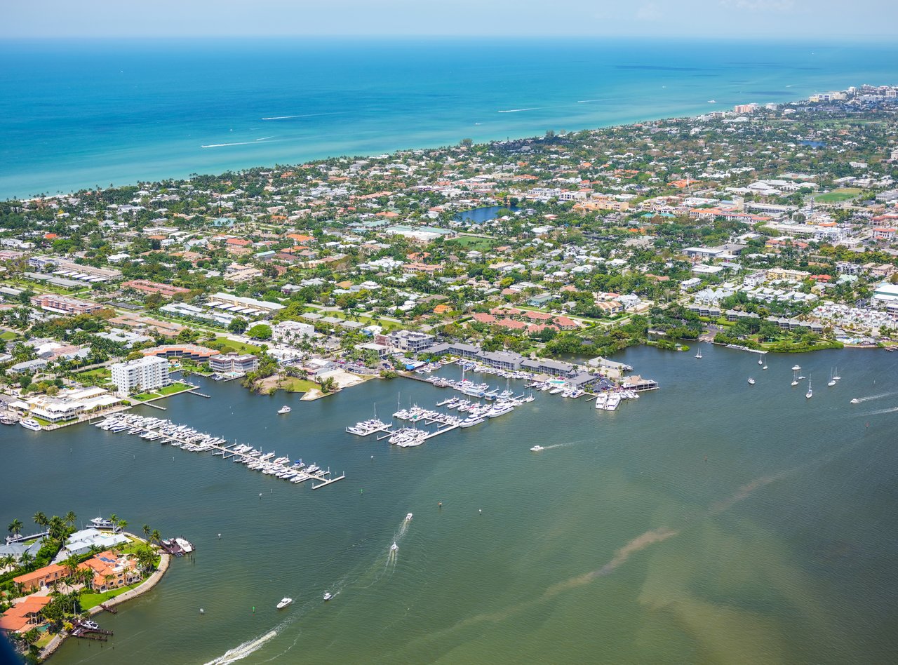 Aerial coastal neighborhood with a marina, docked boats, and turquoise ocean shoreline.