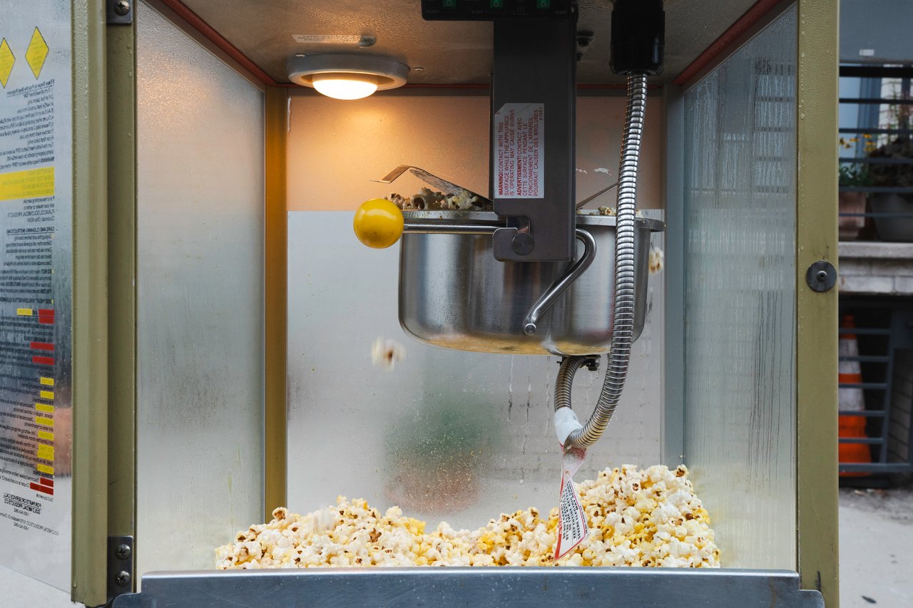 Commercial popcorn machine popping corn, with a yellow handle and fresh popcorn below.