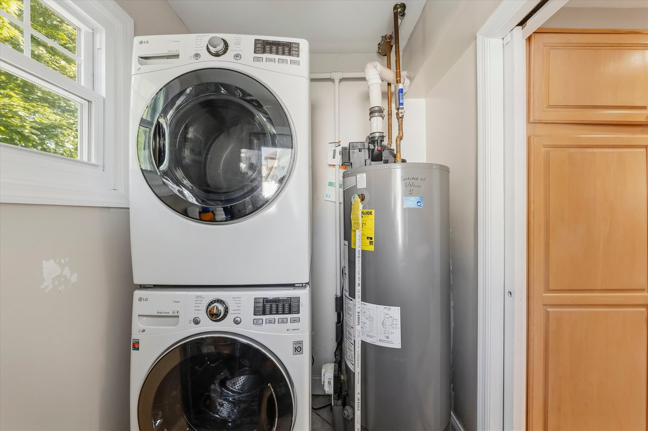 Laundry area with stacked front-loading washer and dryer beside a tall water heater.