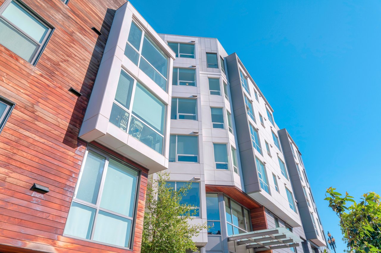 Modern condominium building with white panels, reddish wood siding, and large windows.