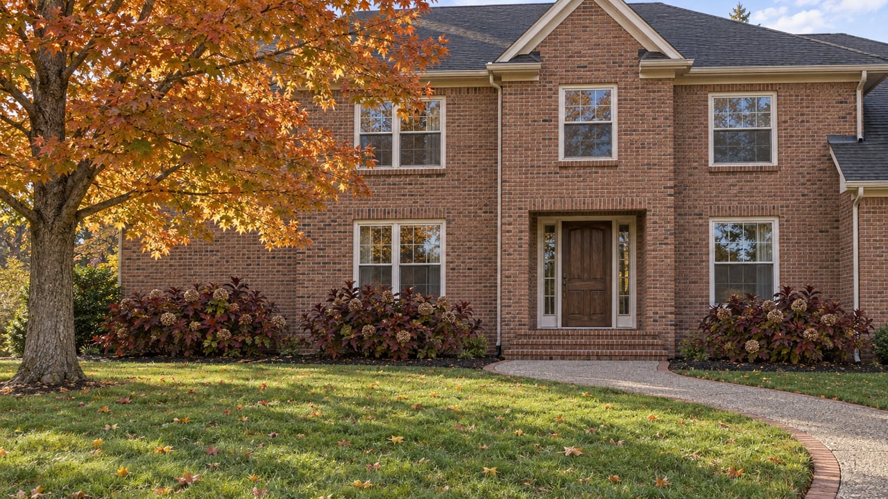 Traditional two-story brick home beyond a deep autumn lawn, with a copper-colored maple and curved front walk.