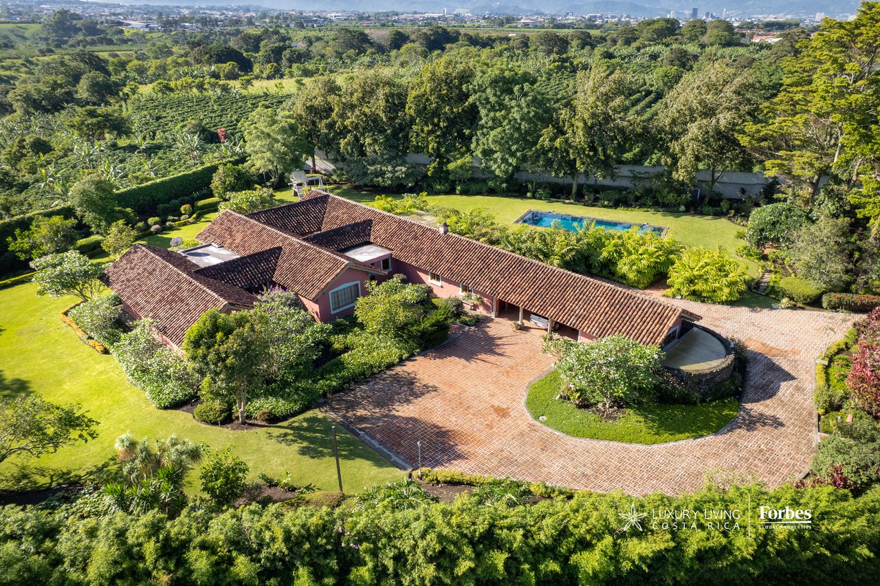 Aerial view of a hacienda estate with red tile roofs, landscaped grounds, and a swimming pool.