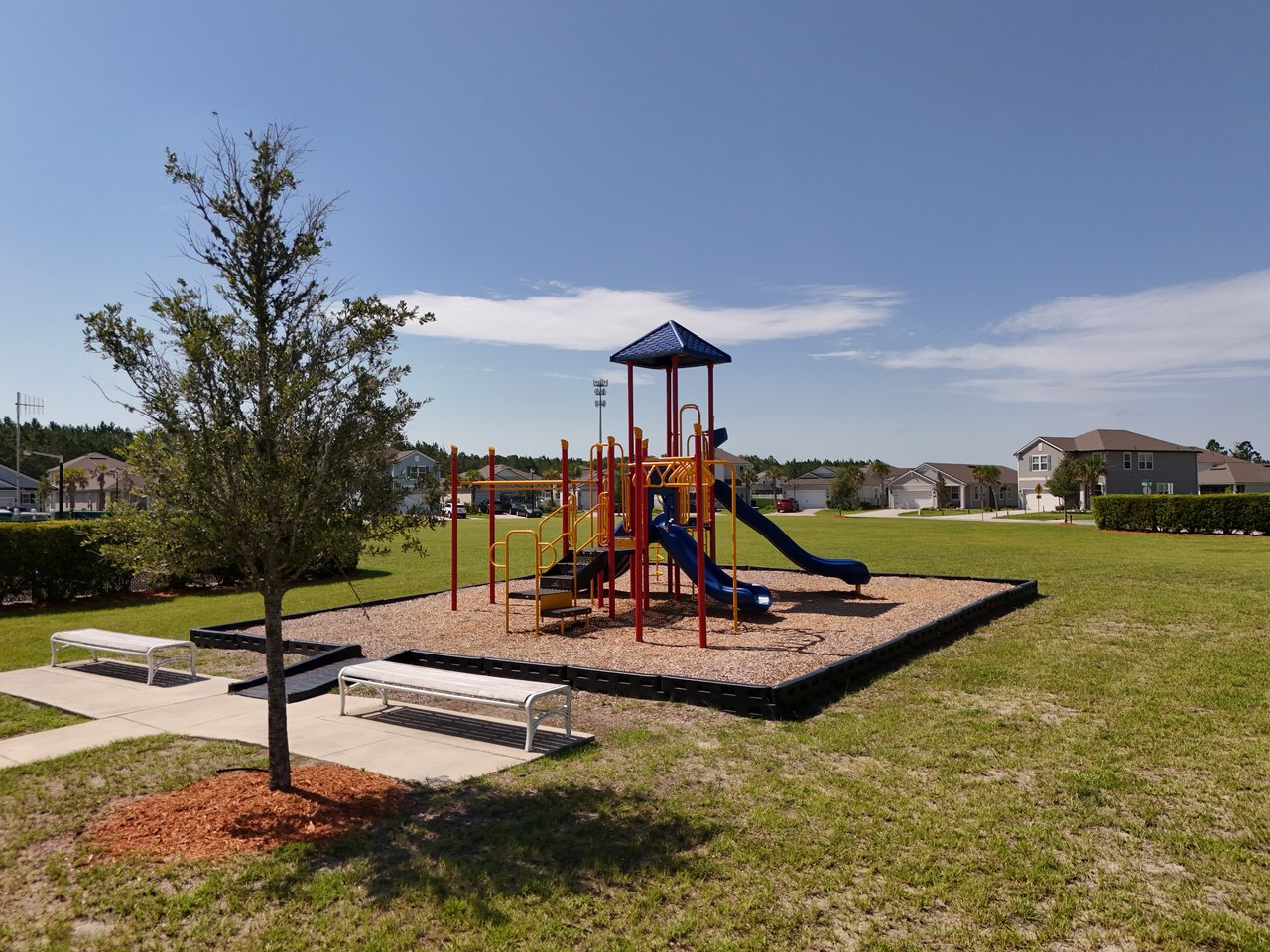 Neighborhood playground with blue slides, benches, and homes in the background.