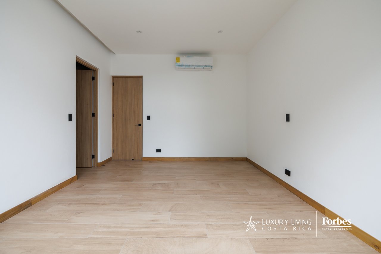 Empty room with pale wood-look tile flooring, wooden doors, and a wall-mounted air conditioner.