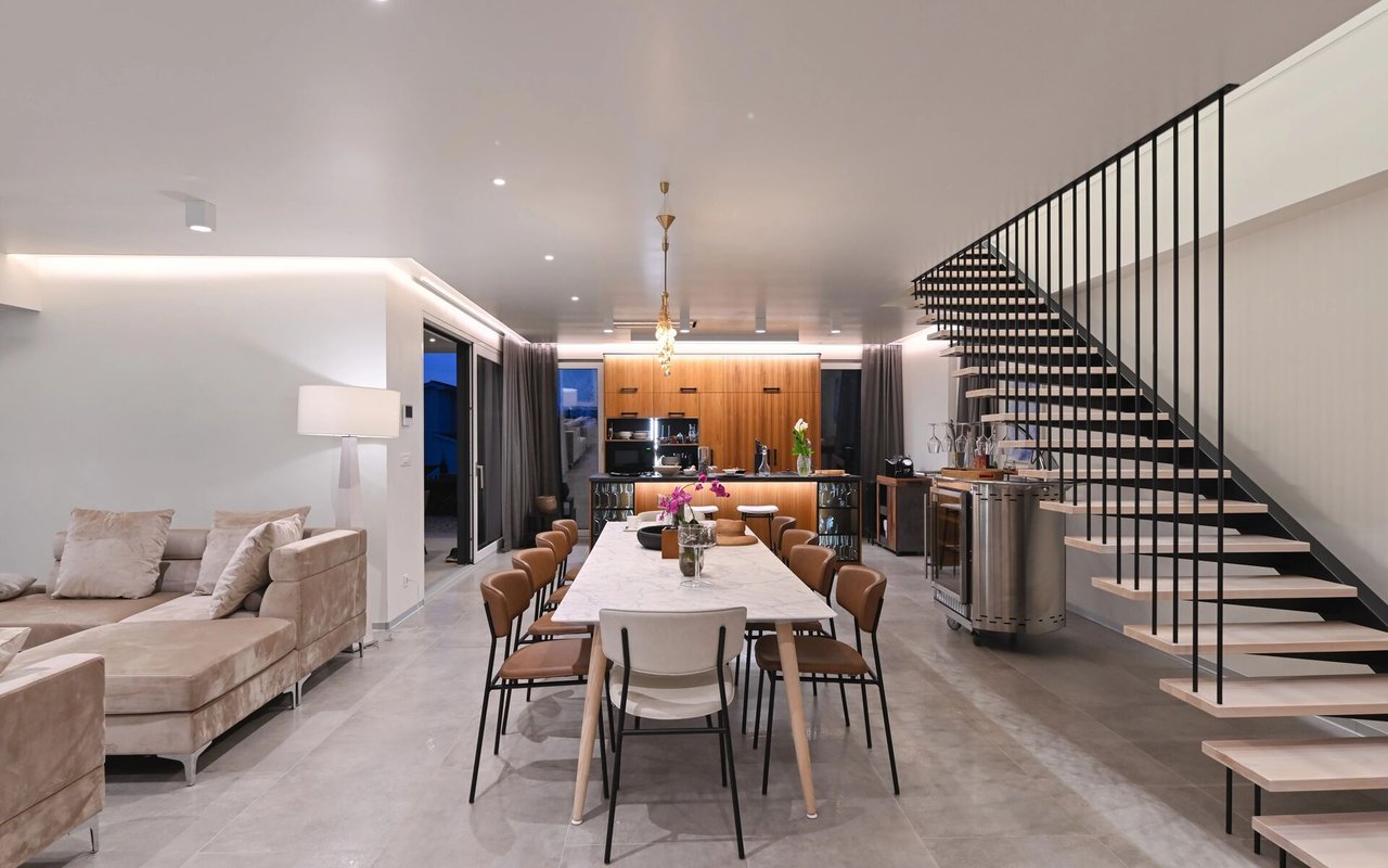 Open-plan living and dining area with a marble table, wood-fronted kitchen, and black open-riser staircase.