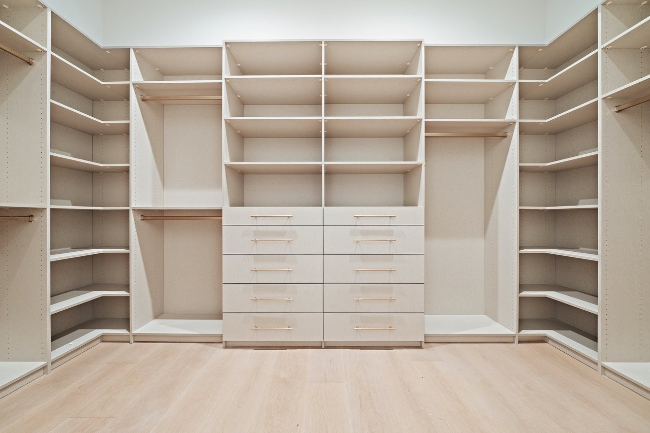 Walk-in closet with pale built-in shelves and a central bank of drawers