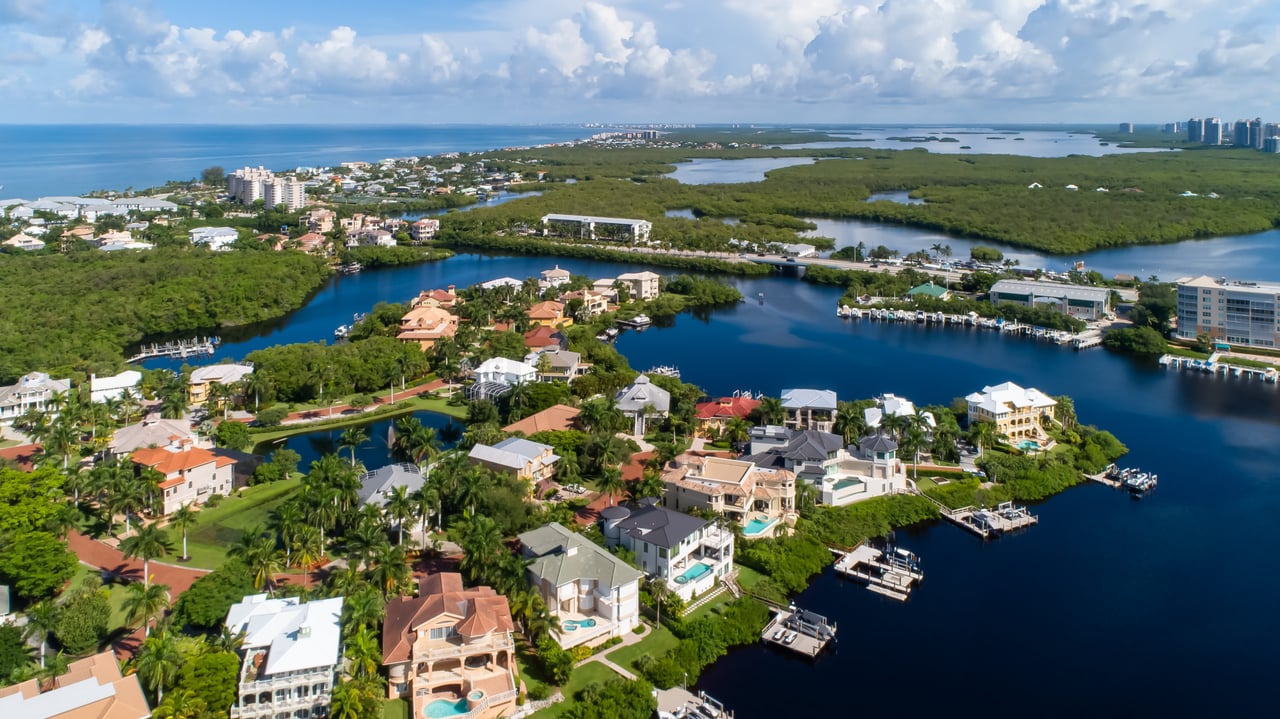 Aerial view of waterfront homes and docks beside blue canals and mangrove wetlands.