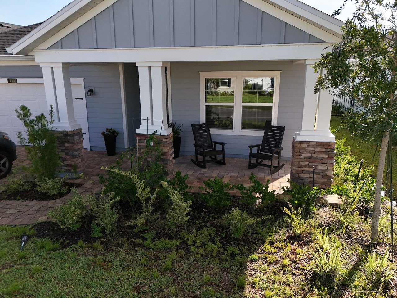Gray home with a covered porch, brick-based columns, and two black rocking chairs.