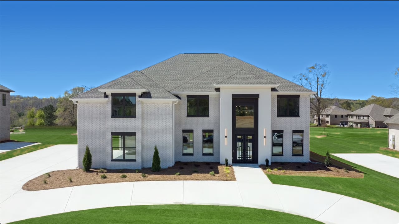 Two-story white-brick house with a tall central entrance, black-framed windows, and a curved concrete driveway.