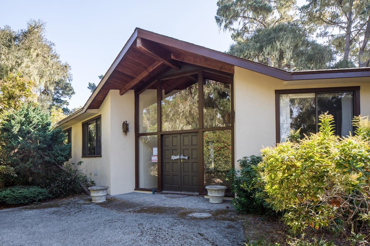 Cream stucco home with a tall timber-framed entry and landscaped front garden.