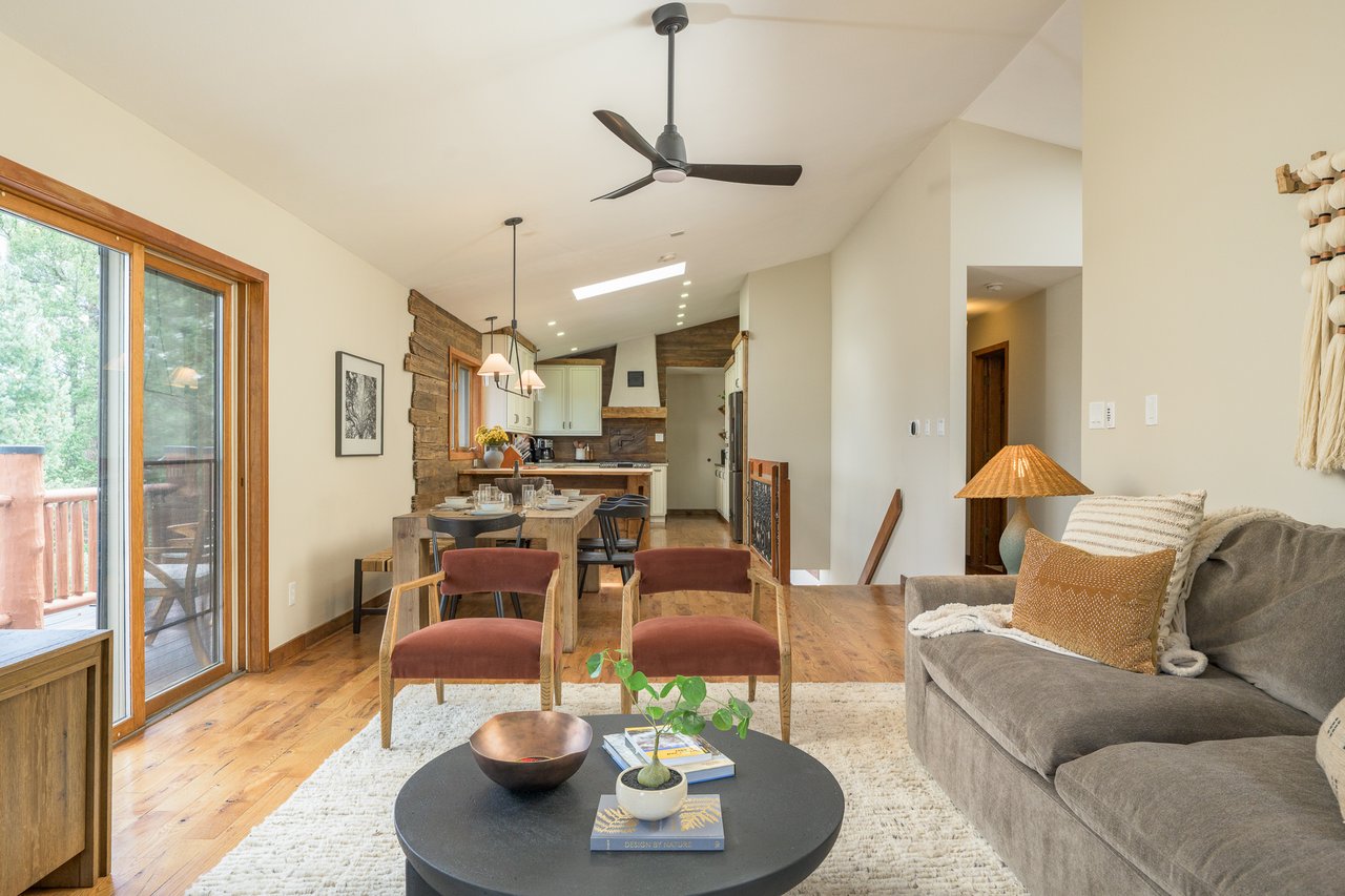 Open-plan living and dining room with wood floors, a reclaimed-wood accent wall, and sliding doors to a deck.
