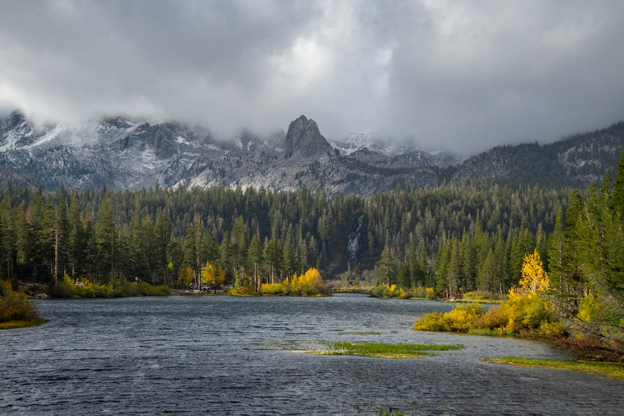River and autumn foliage beneath cloud-covered, snow-dusted mountains.
