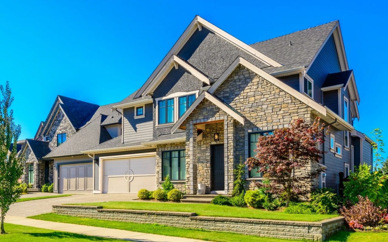 Two-story stone-and-gray-sided home with multiple gables, two garage doors, and landscaped front lawn.