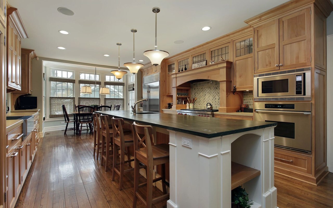 Kitchen with a large dark island, wood cabinetry, stainless appliances, and a window-side dining area.