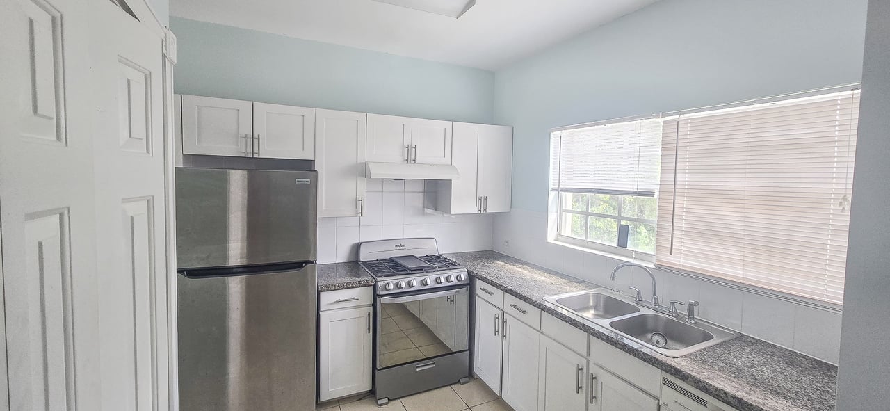 Kitchen with white cabinets, granite counters, stainless appliances, and a double sink beneath a wide window.