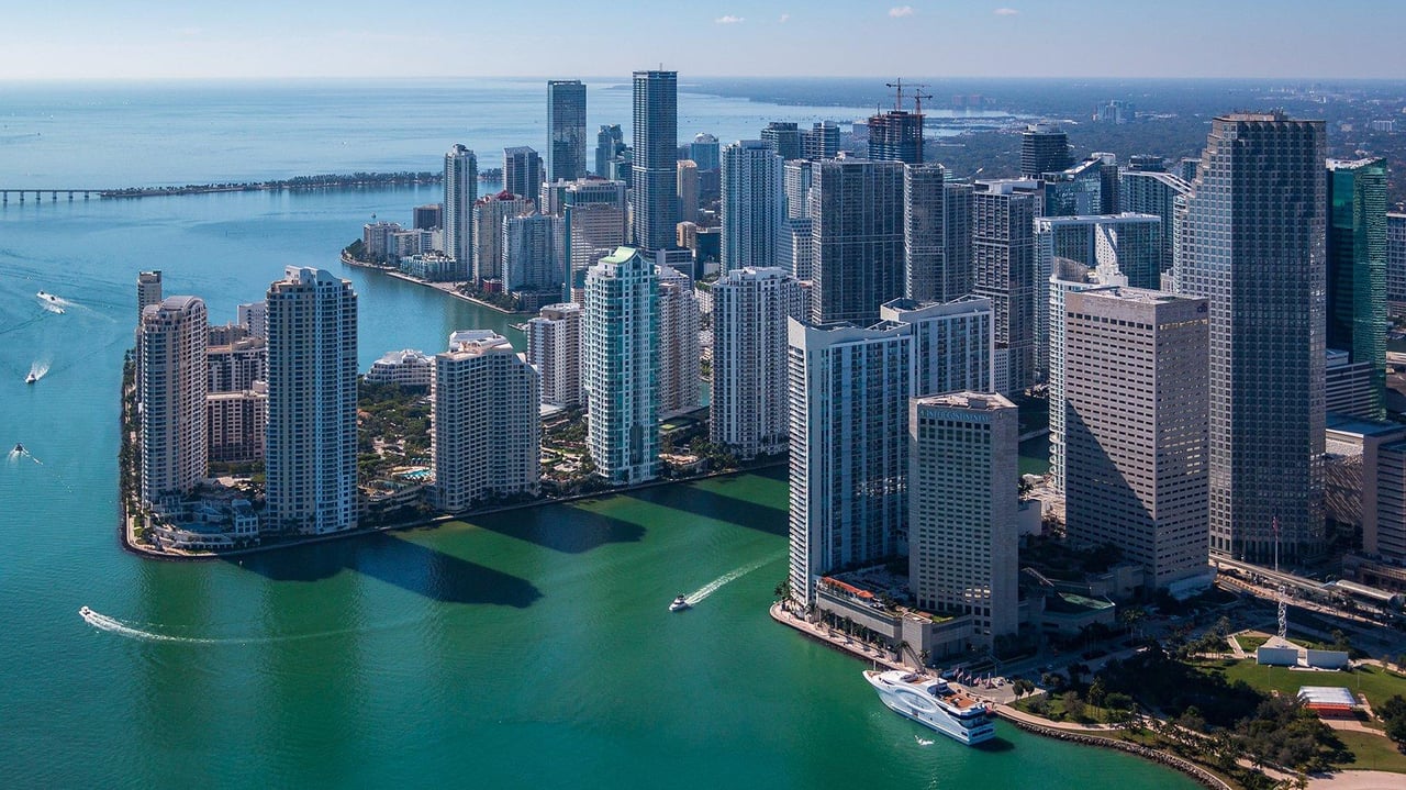 Downtown Miami skyline and waterfront seen from above, with boats crossing Biscayne Bay.