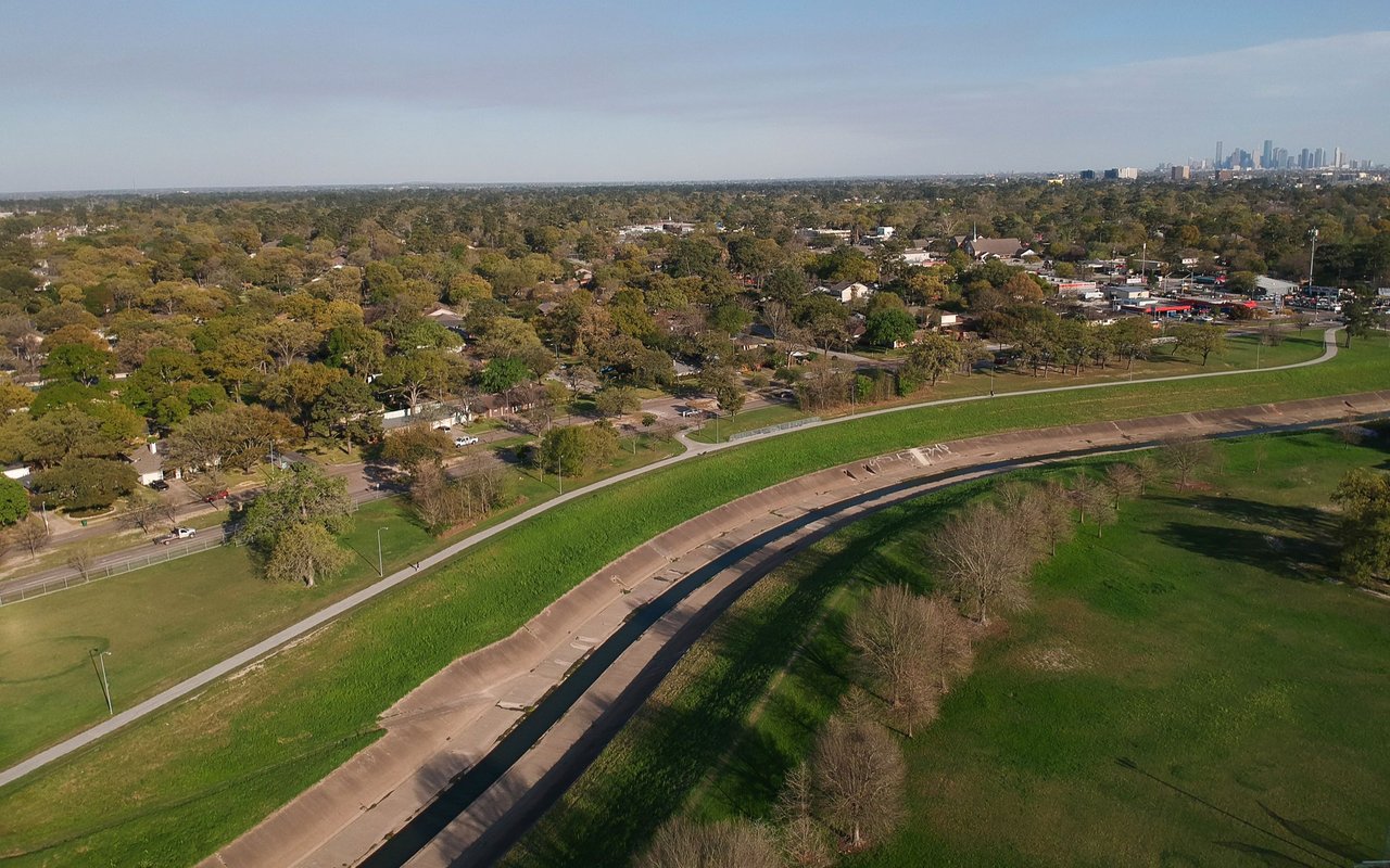 Aerial view of a greenbelt and neighborhood with Houston’s skyline in the distance.