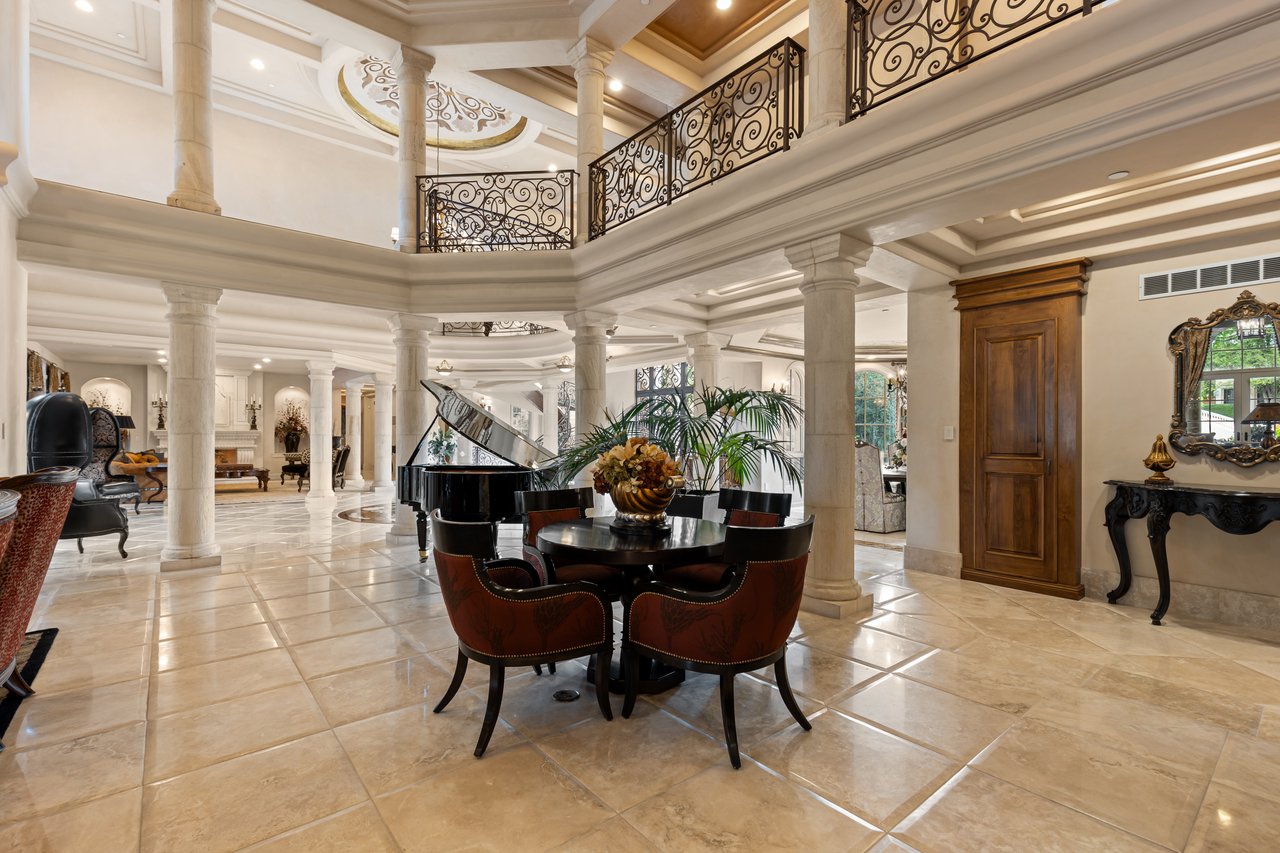 Grand interior with a tiled floor, ornate balcony railings, a grand piano, and a round dining table.